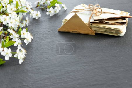 Foto de Stack of old torn vintage letters on yellowed paper against black granite table with cherry blossom branch - Imagen libre de derechos