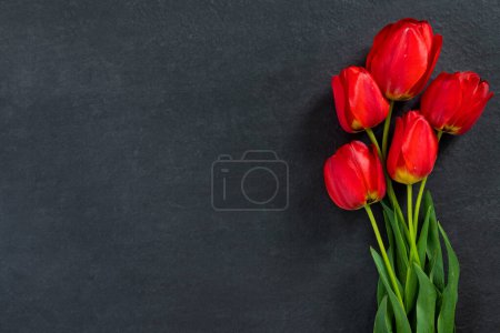 Bouquet of beautiful red tulips on black granite monument with empty space for text