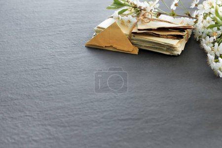 Téléchargez les photos : Stack of old torn vintage letters on yellowed paper against black granite table with cherry blossom branch - en image libre de droit