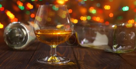 Foto de Vaso de whisky o brandy y botellas vacías en mesa de madera sobre fondo brillante brillante con hermoso bokeh - Imagen libre de derechos