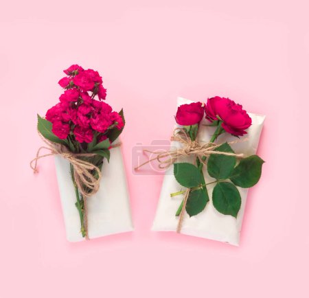 Téléchargez les photos : Ensemble de papier d'emballage et de fleurs pour fait à la main sur fond rose. Cadeaux artisanaux boîte artisanale avec bouquet de roses rouges - en image libre de droit