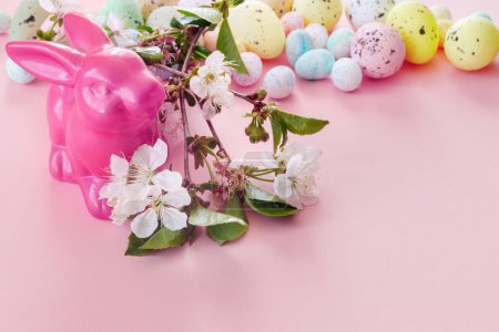 Foto de Rama de sakura floreciente, juguete divertido conejito y huevos de Pascua sobre fondo de papel rosa. - Imagen libre de derechos