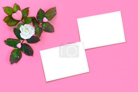 Téléchargez les photos : Belles roses blanches avec feuillage vert et coeur pour la Saint-Valentin sur fond de papier rose. Carte de vœux créative - en image libre de droit