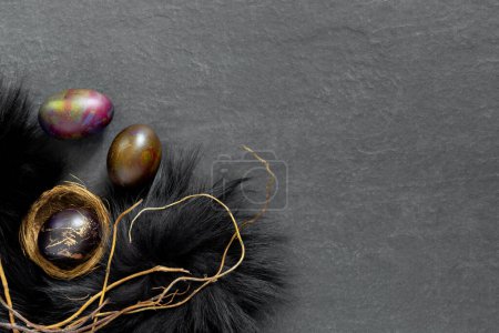 Téléchargez les photos : Nid en fourrure noire avec des œufs peints sur une table en pierre sombre. Bannière festive de Pâques avec des branches. Conception conceptuelle - en image libre de droit