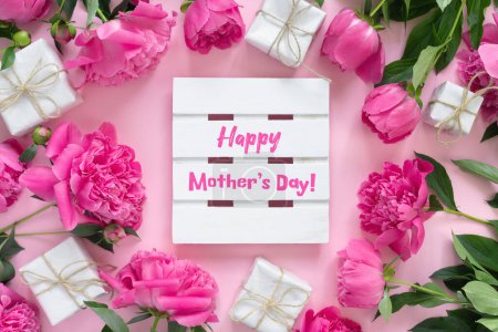 Téléchargez les photos : Bouquet of beautiful pink peonies with gift boxes in paper wrapping. Round frame of flowers. White wooden board with text Happy Mother's Day! - en image libre de droit