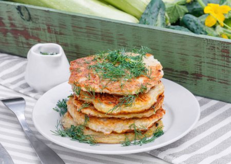 Photo for Delicious pancakes from courgettes and fresh vegetables with sour cream and dill in the garden background - Royalty Free Image