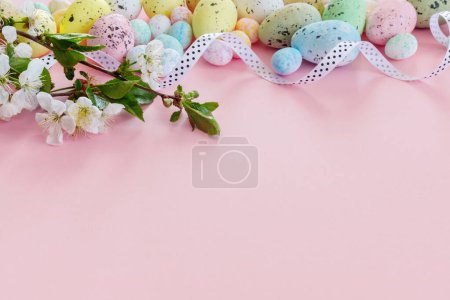 Téléchargez les photos : Belle carte de Pâques avec des œufs colorés et des branches de cerise sur fond rose papier. Carte de vœux florale avec espace de copie pour votre texte. - en image libre de droit