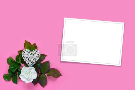 Foto de Hermosas rosas blancas con follaje verde y corazón para el Día de San Valentín sobre fondo de papel rosa. Tarjeta de felicitación creativa - Imagen libre de derechos