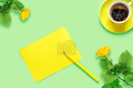 Téléchargez les photos : Bouquet de belles roses jaunes et tasse de café aromatique frais chaud sur fond de papier vert. Feuille de carnet et crayon pour votre texte - en image libre de droit