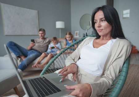Téléchargez les photos : Femme utilisant un ordinateur portable avec intérêt à la maison tandis que l'enfant se détendre sur le canapé - en image libre de droit