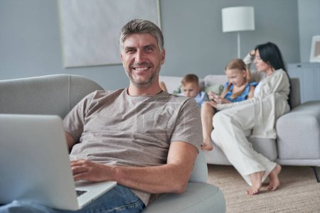 Photo for Portrait of father on sofa, against the background of her happy family at home - Royalty Free Image