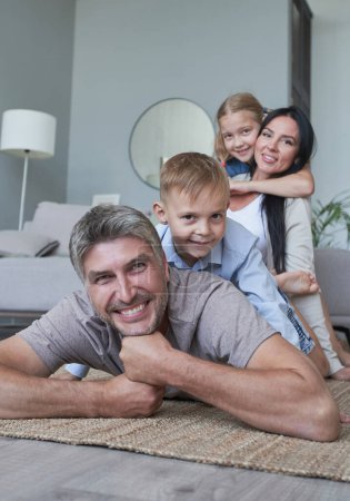 Téléchargez les photos : Jeune famille de quatre personnes qui s'amuse à la maison souriant - en image libre de droit