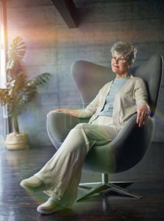 Foto de Atractiva mujer de mediana edad sonriente modelo sentado en silla mirando a la cámara en la oficina - Imagen libre de derechos