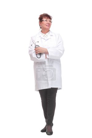 Photo for Side view of serious mature woman doctor in a white coat listens with a stethoscope to an invisible object posing on a white background. Concept of treatment and recovery - Royalty Free Image