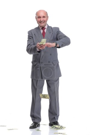 Foto de Hombre de negocios maduro en traje y ropa formal lanzando billetes de banco en dólares de aire aislados sobre fondo blanco - Imagen libre de derechos