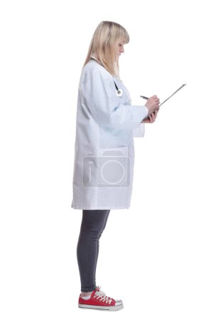 Téléchargez les photos : Vue latérale. jeune femme médecin prenant des notes dans un presse-papiers. isolé sur un fond blanc. - en image libre de droit