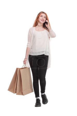 Foto de Retrato de una chica bastante feliz hablando en el teléfono móvil mientras sostiene bolsas de compras y mirando hacia otro lado en el espacio de copia aislado sobre fondo blanco - Imagen libre de derechos