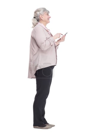Foto de Vista lateral. mujer mayor casual leyendo un mensaje en su teléfono inteligente. aislado sobre un fondo blanco. - Imagen libre de derechos