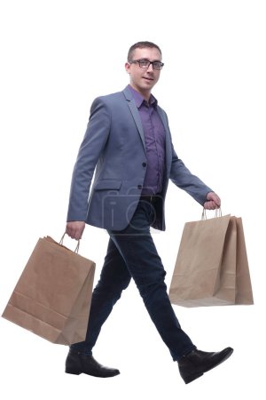 Young businessman wearing jeans and glasses with shopping bags walking against a white background.