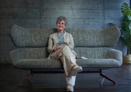 Foto de Visión, edad y concepto de personas - retrato de la mujer mayor feliz en gafas sentado en el sofá en casa - Imagen libre de derechos