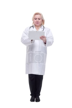 Téléchargez les photos : Médecin féminin portant un manteau blanc et utilisant une tablette numérique, regardant l'écran avec une expression sérieuse - en image libre de droit