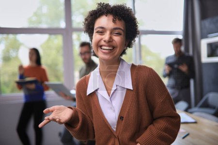 Foto de Exitosa mujer de negocios de pie en la oficina creativa y mirando a la cámara mientras sonríe - Imagen libre de derechos