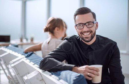 Téléchargez les photos : Jeune homme d'affaires avec une tasse de café assis dans un bureau moderne. pause café - en image libre de droit