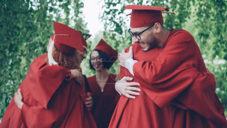 Photo for Excited young people graduating students in bright formal gowns and hats are hugging congratulating each other on graduation, laughing and celebrating end of academic year. - Royalty Free Image