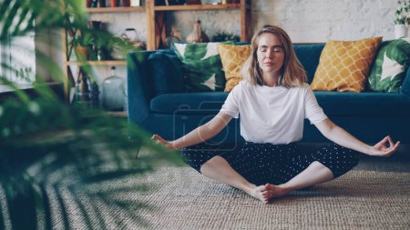 Téléchargez les photos : La jeune femme flexible se relaxe en position Badha Konasana en pratiquant la posture de yoga papillon à la maison en profitant du repos et de la détente. Concept de bien-être, d'intérieur et de personnes
. - en image libre de droit