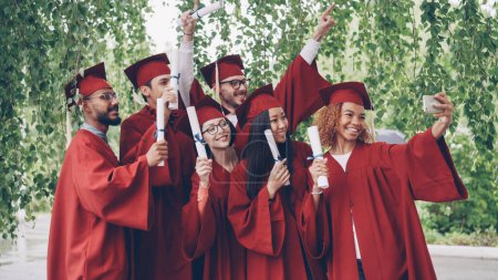 Photo for Excited graduating students are taking selfie with smartphone, young people are waving diplomas, posing, smiling and laughing. Education, youth and success concept. - Royalty Free Image