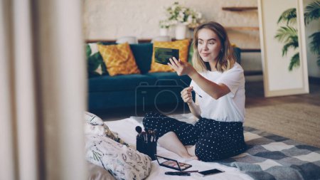Téléchargez les photos : Charmante jeune femme peint les sourcils se maquiller le matin assis sur le lit dans un appartement moderne. Kit cosmétique, ensemble professionnel de brosses et bel intérieur est visible
. - en image libre de droit