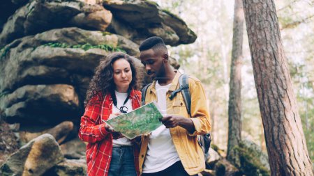 Photo for Lost tourists are standing in forest near huge rocks, looking at map and talking discussing way to their destination place. People and nature concept. - Royalty Free Image