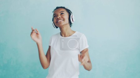 Foto de Retrato de una mujer afroamericana feliz escuchando música a través de auriculares inalámbricos y bailando disfrutando de la melodía. Tecnología moderna, gente joven y concepto divertido
. - Imagen libre de derechos
