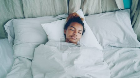 Foto de Mujer afroamericana joven está durmiendo en la cama cómoda bajo una manta caliente que descansa sobre ropa de cama hermosa. Confort, descanso de las personas y el concepto de dormitorio
. - Imagen libre de derechos