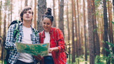 Foto de Los turistas perdidos están de pie en el bosque mirando el mapa, hablando y haciendo gestos para encontrar el camino. Gente, viaje y hermoso concepto de la naturaleza. - Imagen libre de derechos