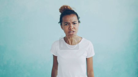 Foto de Retrato de una mujer afroamericana enojada hablando y haciendo gestos expresando emociones negativas de pie sobre un fondo azul claro. Sentimientos, reacciones y concepto de personas. - Imagen libre de derechos