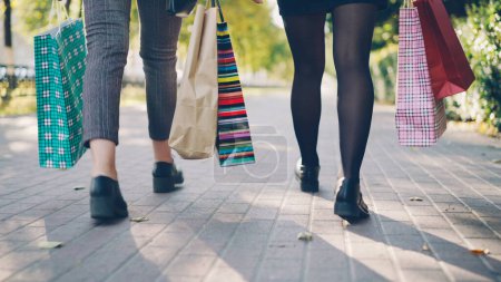 Téléchargez les photos : Plan à angle bas des jambes des femmes marchant dans la rue avec des sacs en papier colorés après une journée bien remplie dans les magasins. Jeunes, loisirs, shopping et amitié conccept
. - en image libre de droit