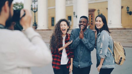 Foto de Grupo multiétnico de turistas extranjeros está tomando fotos posando para la cámara y divertirse abrazando y riendo de pie en la calle en la hermosa ciudad en el día de verano. - Imagen libre de derechos