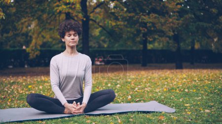 Photo for Flexible young lady is sitting on mat in yoga pose enjoying fresh air, peace and relaxation. Healthy lifestyle for urban people, active youth and autumn nature concept. - Royalty Free Image