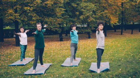 Photo for Young women are doing yoga standing in warrior pose Virabhadrasana then moving into triangle position Trikonasana during outdoor class in local park. Youth and health concept. - Royalty Free Image