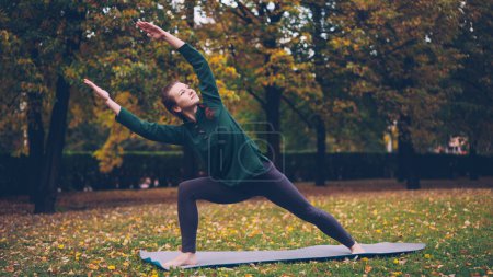 Téléchargez les photos : Jeune femme mince fait du yoga en plein air changer asanas et profiter du mouvement, l'air frais et belle nature d'automne. Millennials, mode de vie sain et concept de loisirs
. - en image libre de droit