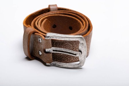 Photo for A rolled-up brown leather belt with a metal buckle on a white table. Copy space - Royalty Free Image