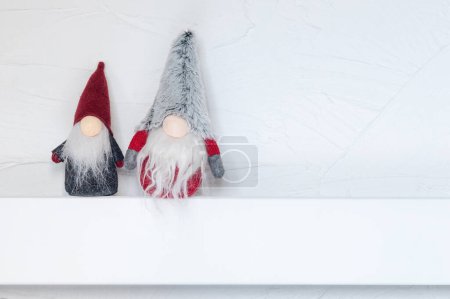 Téléchargez les photos : Elfes, décorations de Noël. Gonks de Noël assis sur une étagère en bois blanc contre le mur. Noel et Nouvel An concept, carte de voeux, espace de copie - en image libre de droit