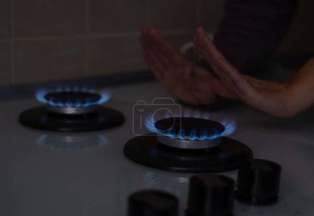 Téléchargez les photos : Une femme se réchauffe les mains à la cuisinière à gaz à la maison. Manque d'électricité et de chaleur dans les maisons des citoyens. Crise énergétique, conséquences des hostilités, guerre en Ukraine - en image libre de droit