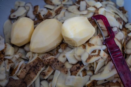 Foto de Las patatas frescas pelan y las patatas, un cuchillo pequeño vegetal. Pelado y listo para cocinar patatas. Residuos biodegradables domésticos. Vista superior - Imagen libre de derechos