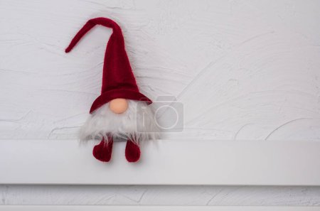 Téléchargez les photos : Gonk scandinave au chapeau rouge. Gnome de Noël sur l'étagère en bois blanc. Espace libre pour le texte. Noel ou Nouvel An concept, carte de voeux - en image libre de droit