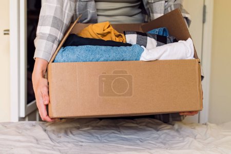 Woman's hands holding a box full of clothes. Home organization and cleaning, reuse and sustainable lifestyle,