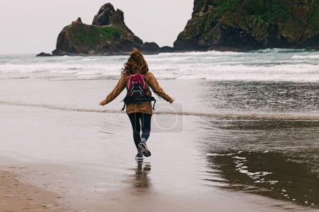 Woman traveler on Oregon Pacific coast at rainy day. Running on the beach, windy weather, view from the back