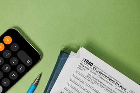 Tax season flat lay on green background. US individual tax form, pencil, smart phone glasses, top view