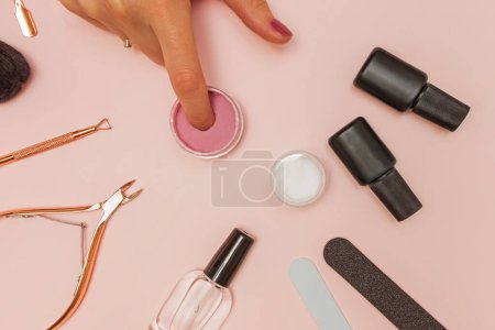 Dipping powder manicure tools on pink background. Woman dip her finger nail in the colorful powder